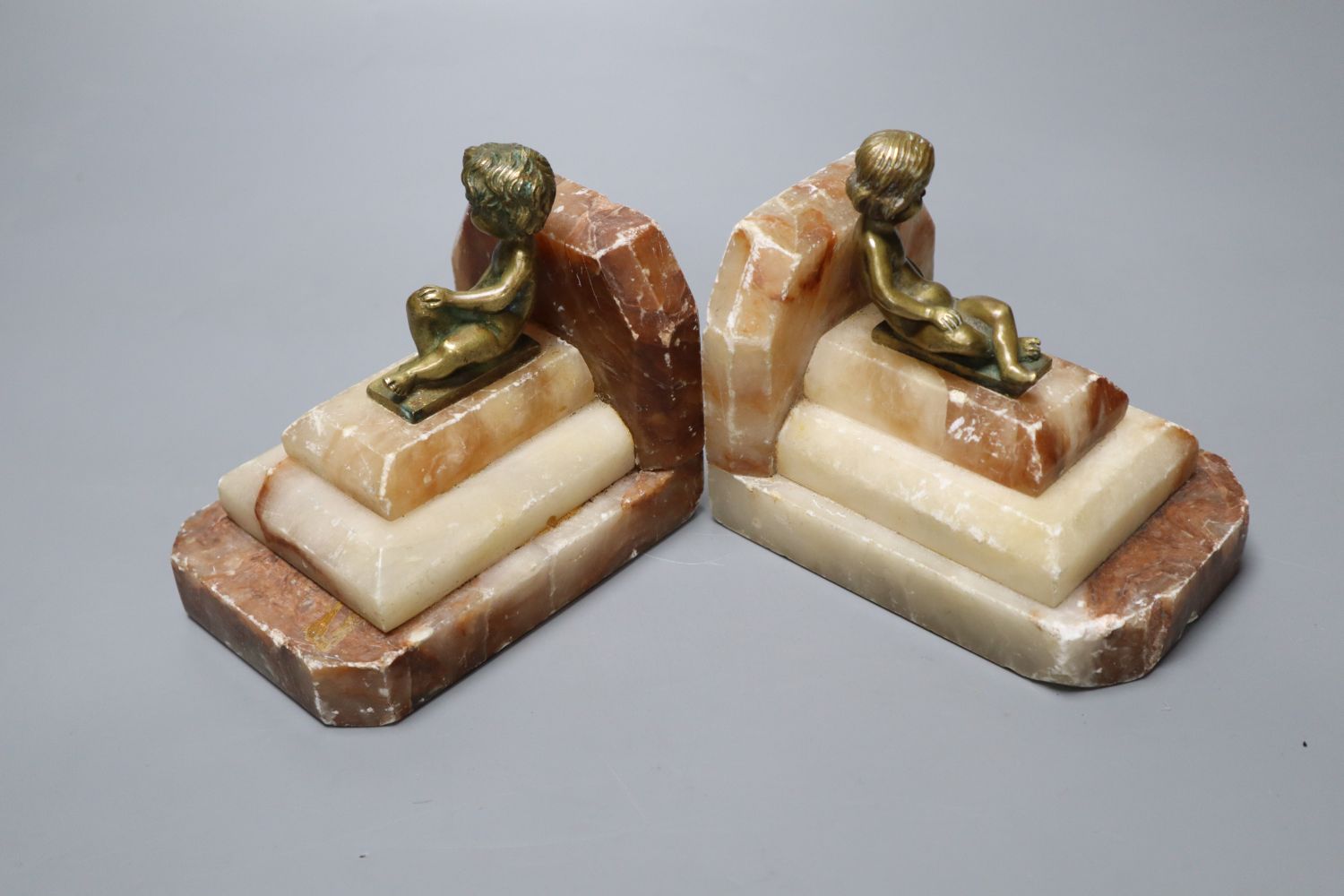 A pair of 1930s stepped marble book-ends, with seated youth surmounts, height 10cm